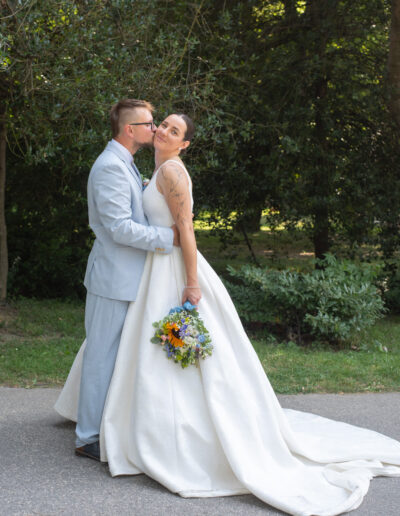 Nevesta a ženích sa držia za ruky počas západu slnka, usmievajú sa a stoja na lúke so zlatým svetlom v pozadí.