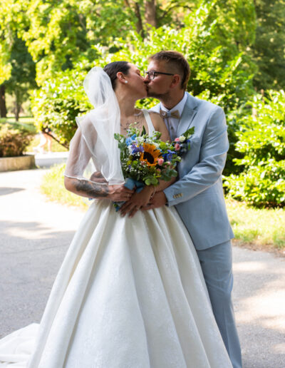 Nevesta a ženích sa držia za ruky počas západu slnka, usmievajú sa a stoja na lúke so zlatým svetlom v pozadí.