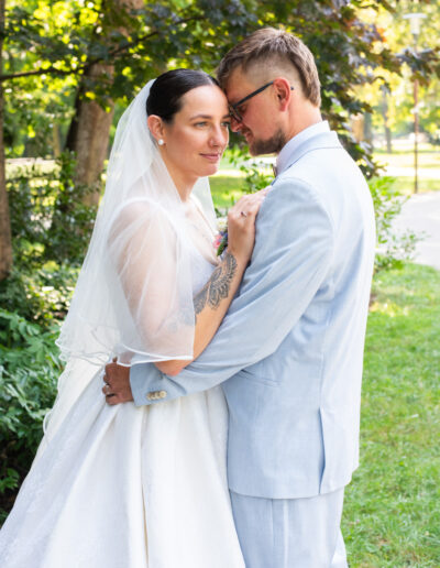 Nevesta a ženích sa držia za ruky počas západu slnka, usmievajú sa a stoja na lúke so zlatým svetlom v pozadí.