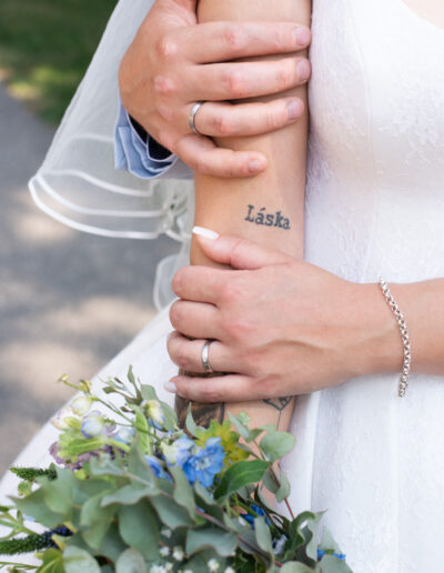 Nevesta a ženích sa držia za ruky počas západu slnka, usmievajú sa a stoja na lúke so zlatým svetlom v pozadí.