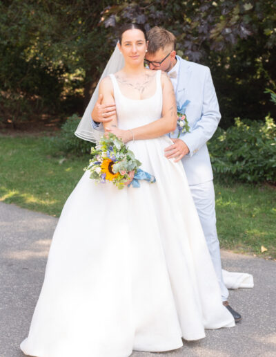 Nevesta a ženích sa držia za ruky počas západu slnka, usmievajú sa a stoja na lúke so zlatým svetlom v pozadí.