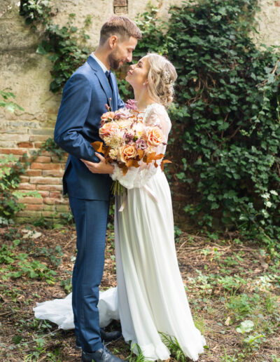 Svadobná fotografia nevesty a ženícha počas západu slnka na lúke, romantický portrét novomanželov v zlatom svetle počas svadobného dňa.