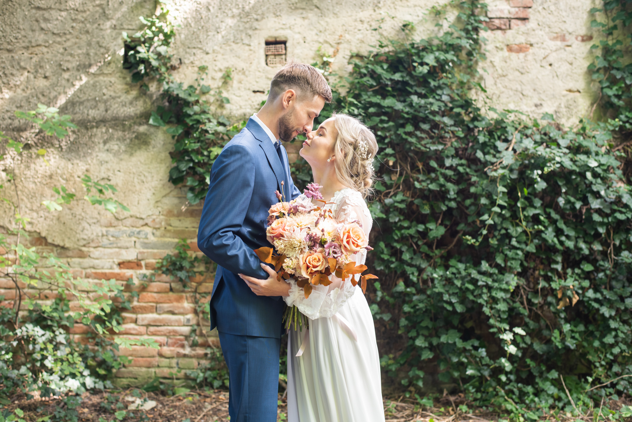 Nevesta v bielych šatách objíma ženícha pred historickou budovou, obaja majú radostný výraz.